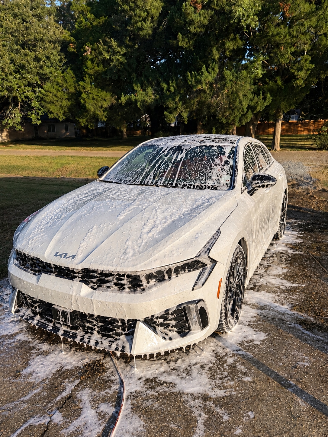 White Kia K5 covered in soap foam during an exterior wash