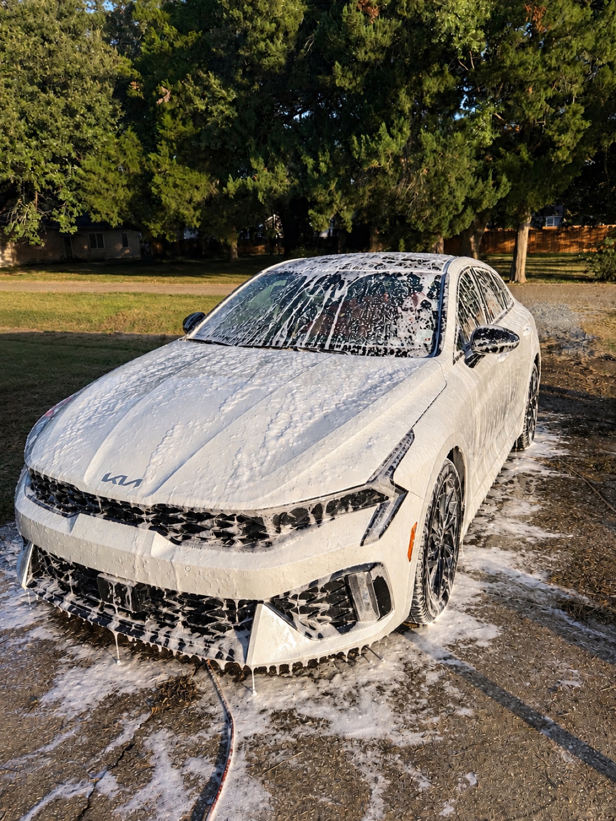 White Kia K5 covered in soap foam during an exterior detail